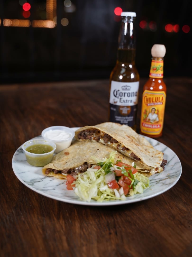 Two quesadillas with meat and cheese, salsa, sour cream, salad, a Corona, and Cholula hot sauce.