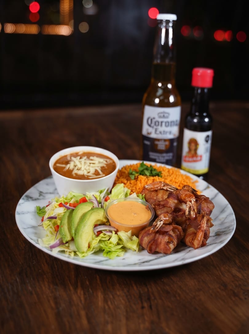 Bacon-wrapped shrimp, rice, beans, and salad with avocado, served with a Corona beer.