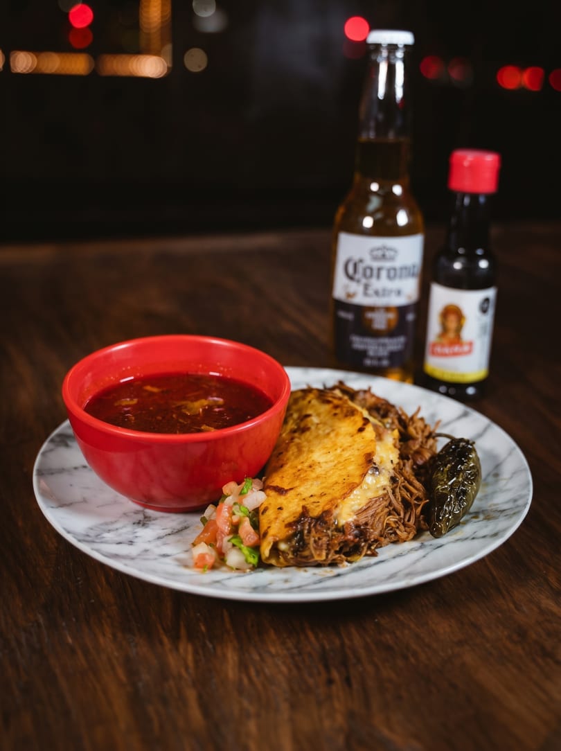 Birria tacos with consommé, pico de gallo, a grilled jalapeño, and a Corona beer.