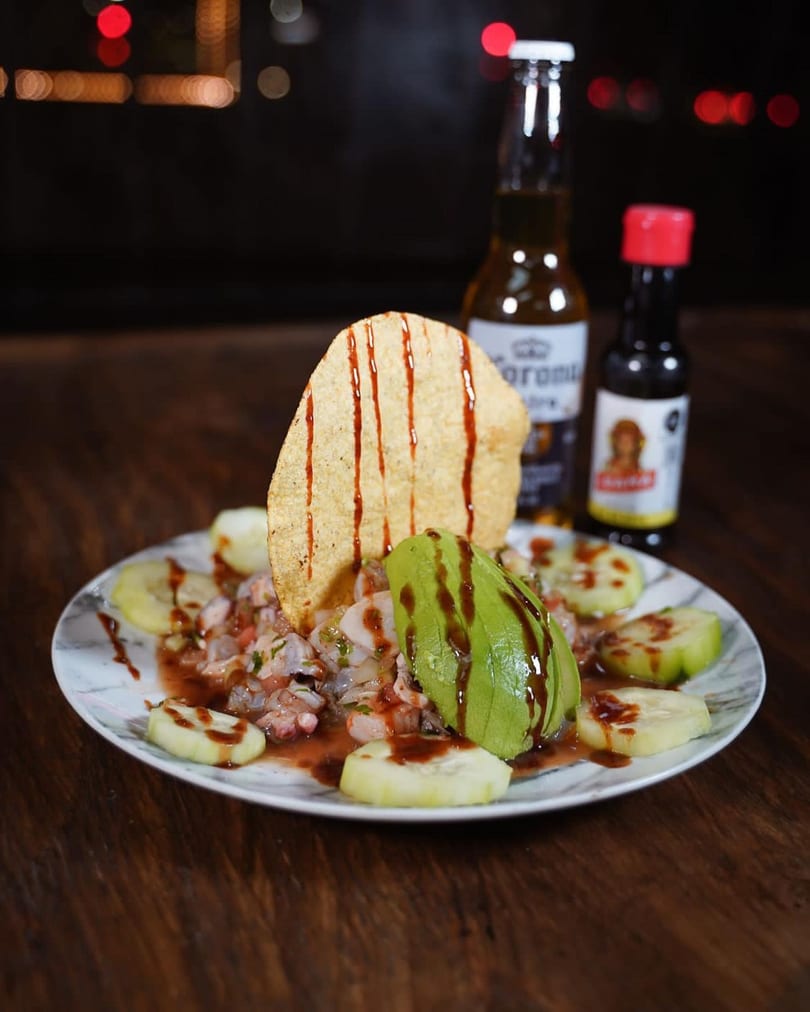 Ceviche with avocado, cucumber, and a tostada, served with a Corona beer and hot sauce.
