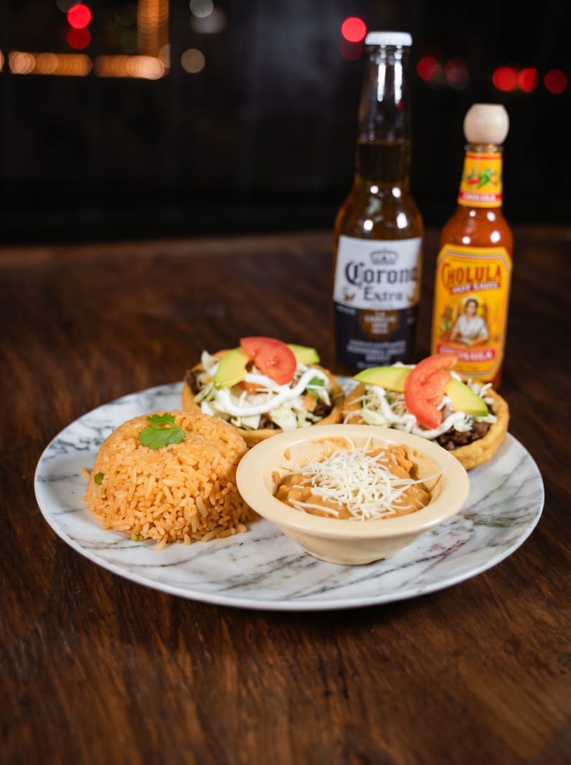 Plate with two sopes, Mexican rice, refried beans, a Corona beer, and Cholula hot sauce.